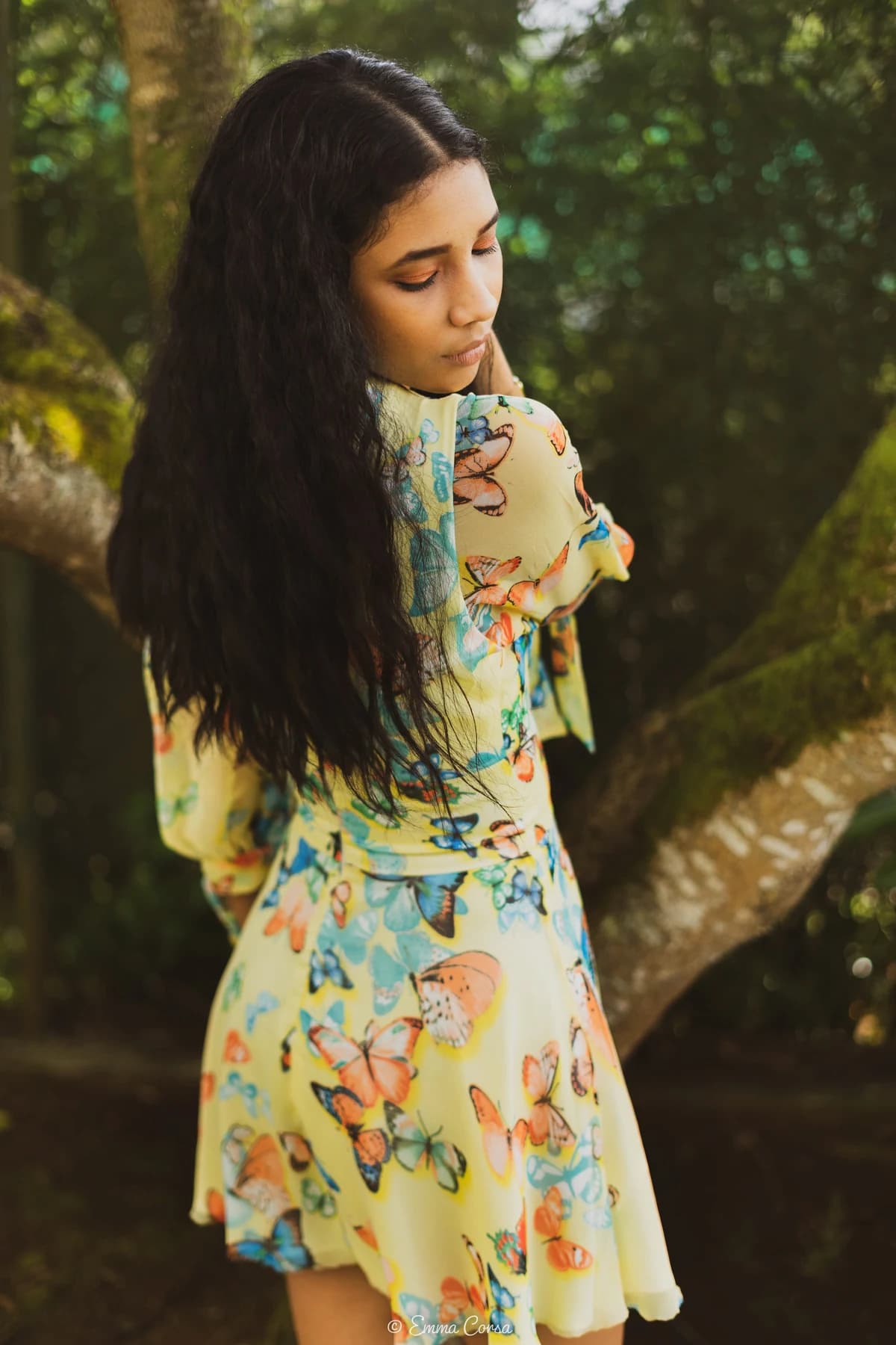 Portrait of a woman in a butterfly-print outfit beneath the trees, with the original Emma Corsa watermark